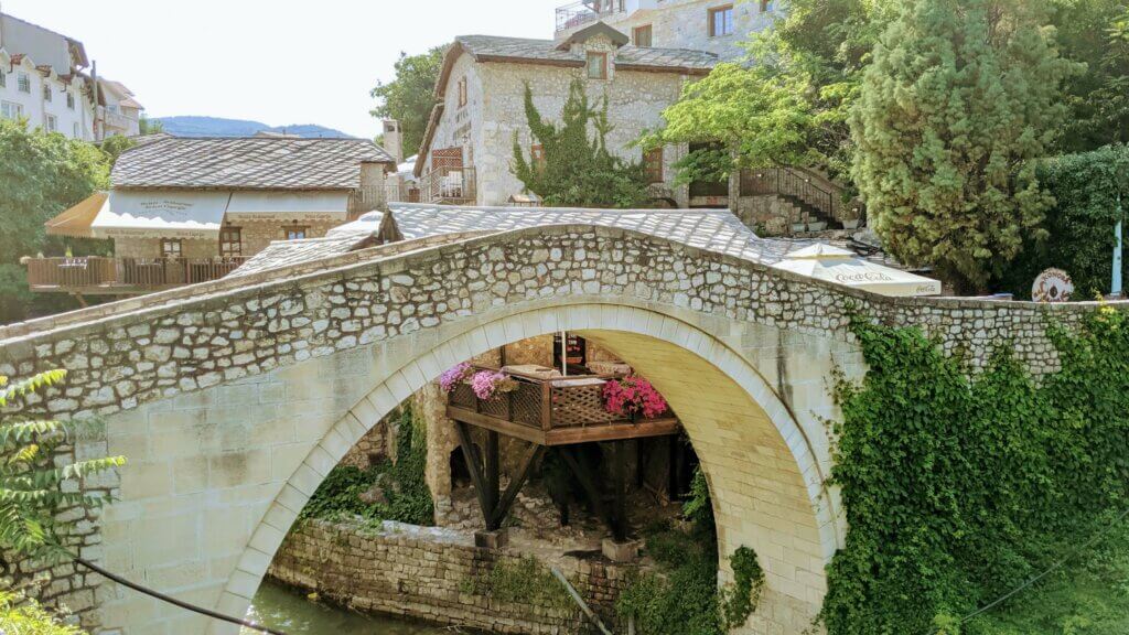 Crooked Bridge bathed in sunlight with cafes in the background is a reason to visit Mostar