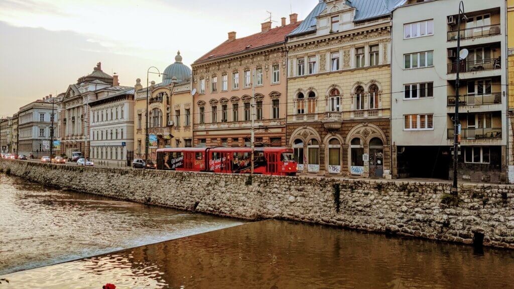 Sarajevo along the River Miljacka with a red tram in front of some buildings